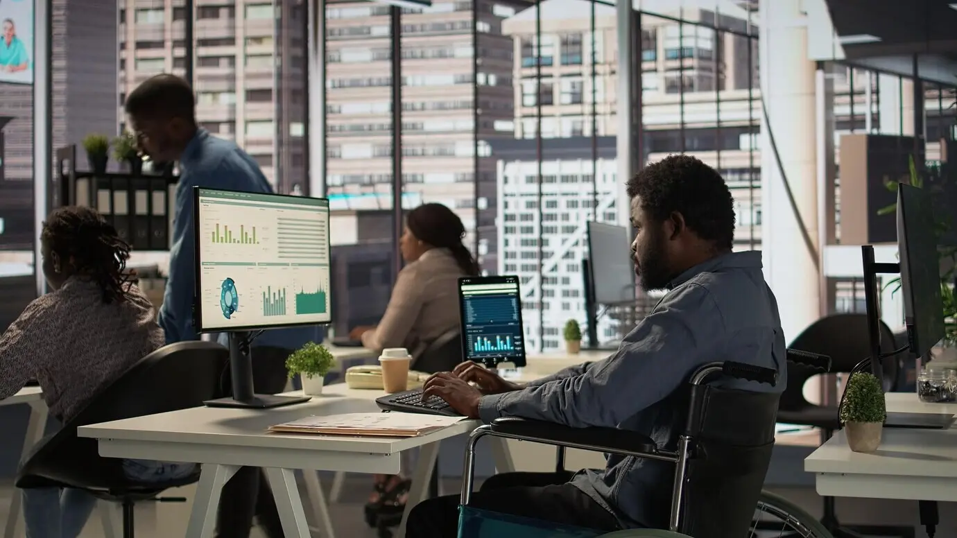 Un employé afro-américain en fauteuil roulant essayant de résoudre des tâches quotidiennes au bureau.