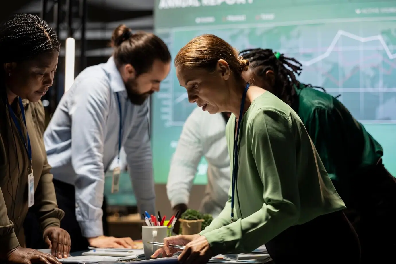 Après les heures de bureau, une équipe aux profils variés collabore à un briefing d’entreprise en s’appuyant sur des projections et